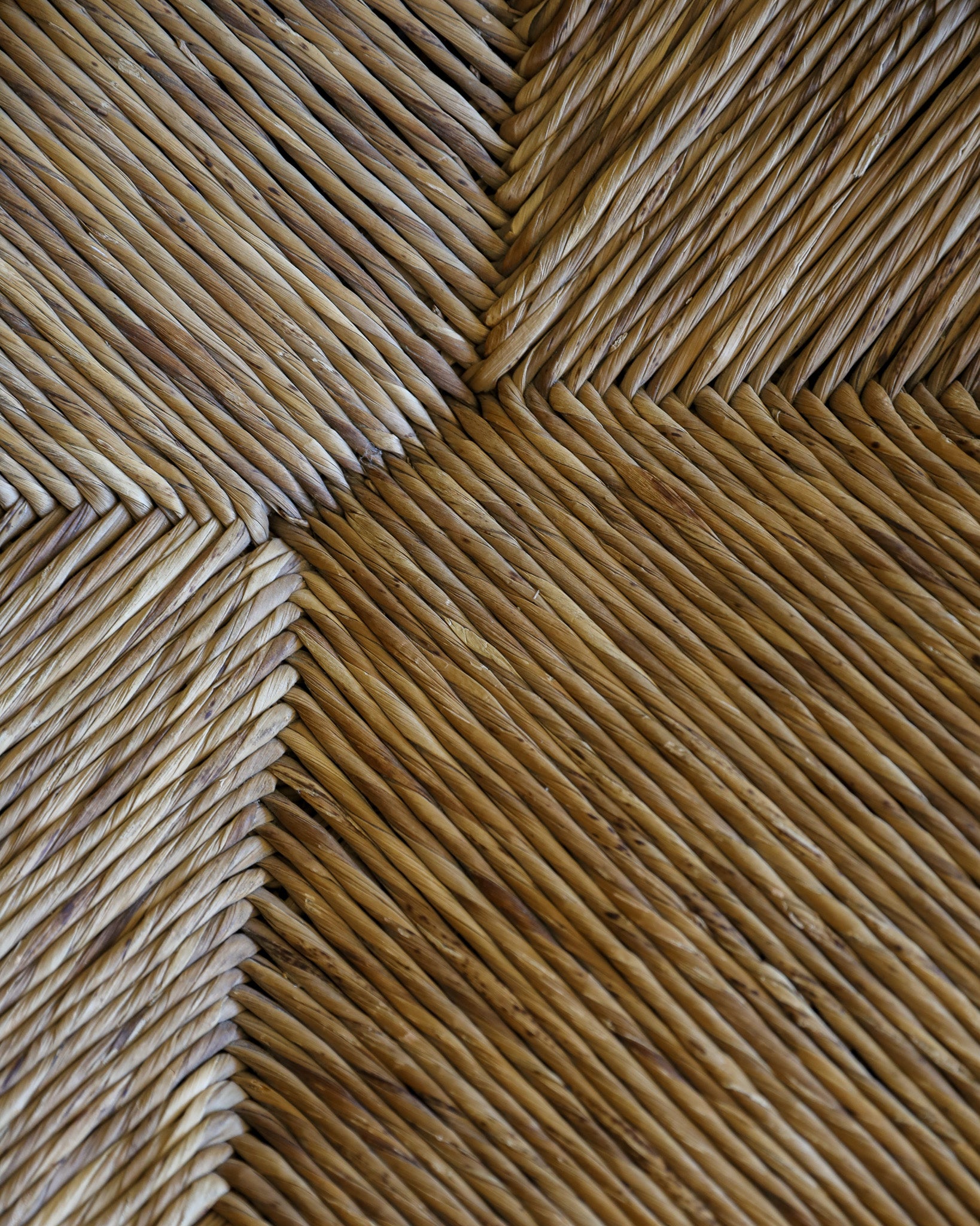 Close-up of a woven natural fiber surface with a herringbone pattern in warm tan and brown tones.
