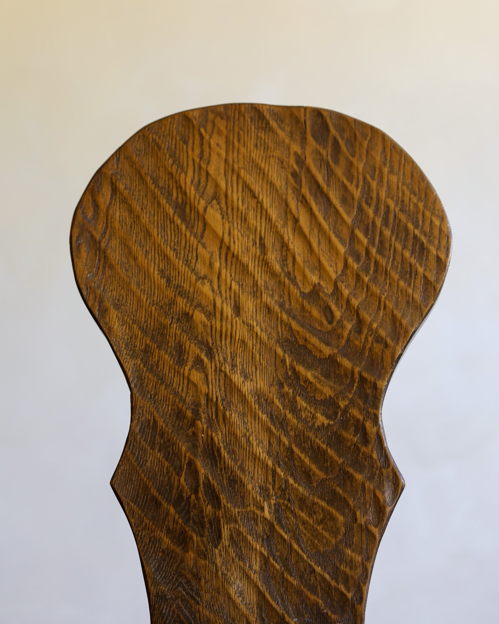 A close-up of a dark brown wooden chair with a prominent wavy grain pattern, shown against a plain off-white background.