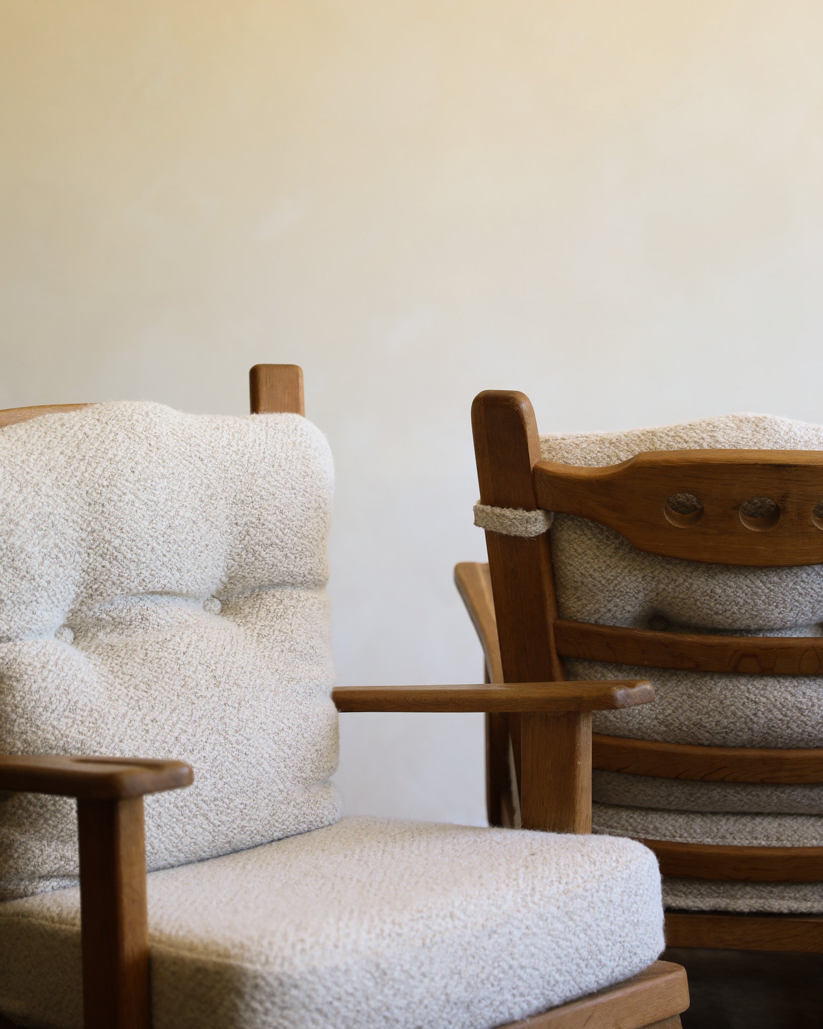 Two wooden chairs with tufted bouclé cushions in a neutral indoor setting with a brown rug and plain wall.