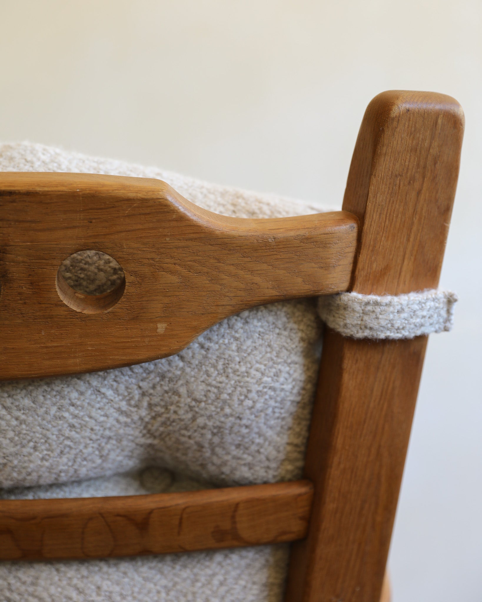 Close-up of a wooden chair with a textured light beige upholstered seat and back, showing the wood grain and a looped fabric detail.