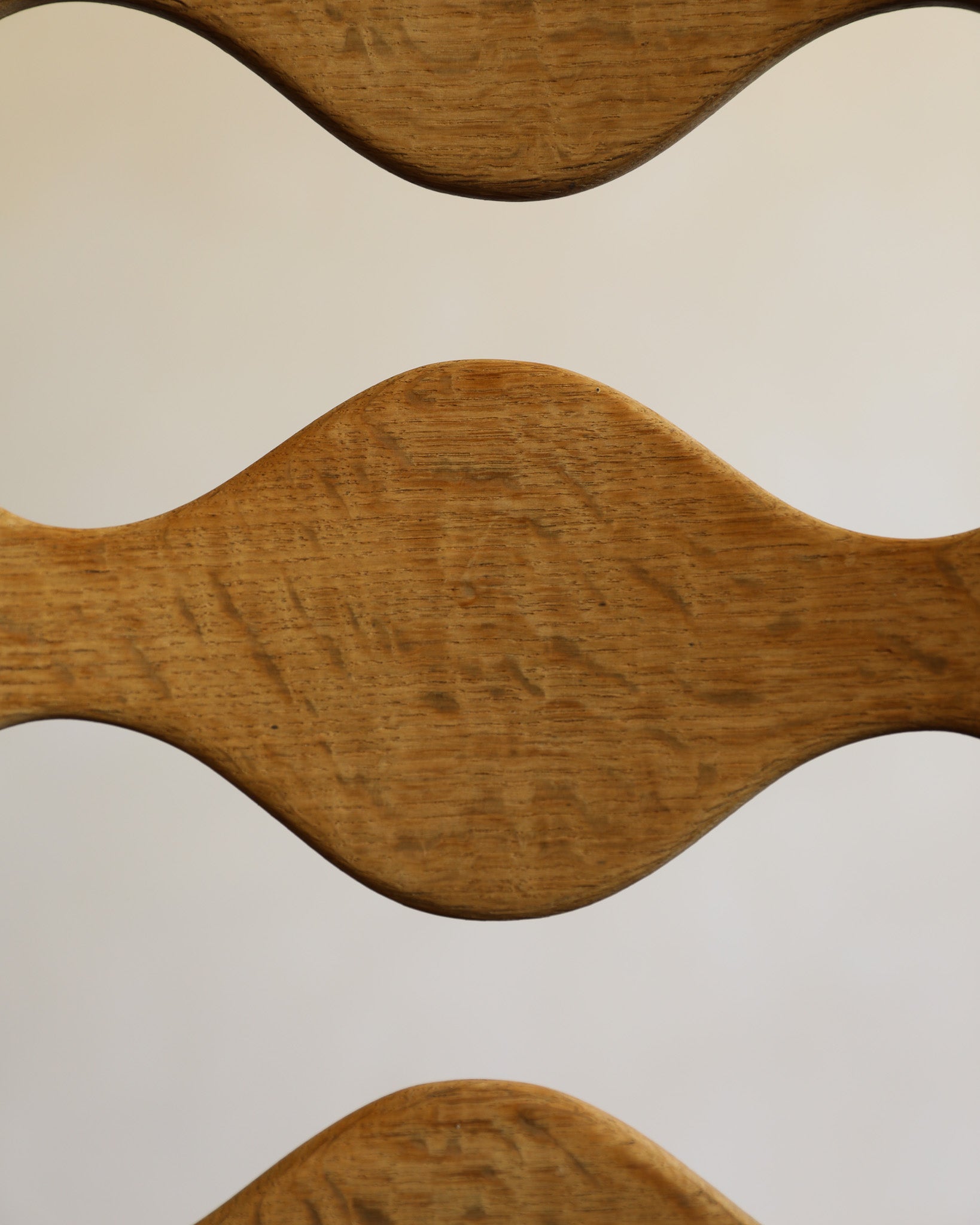 A close-up of a wavy wooden chair back or seat slat, showing the natural grain of medium brown wood against a plain light background.