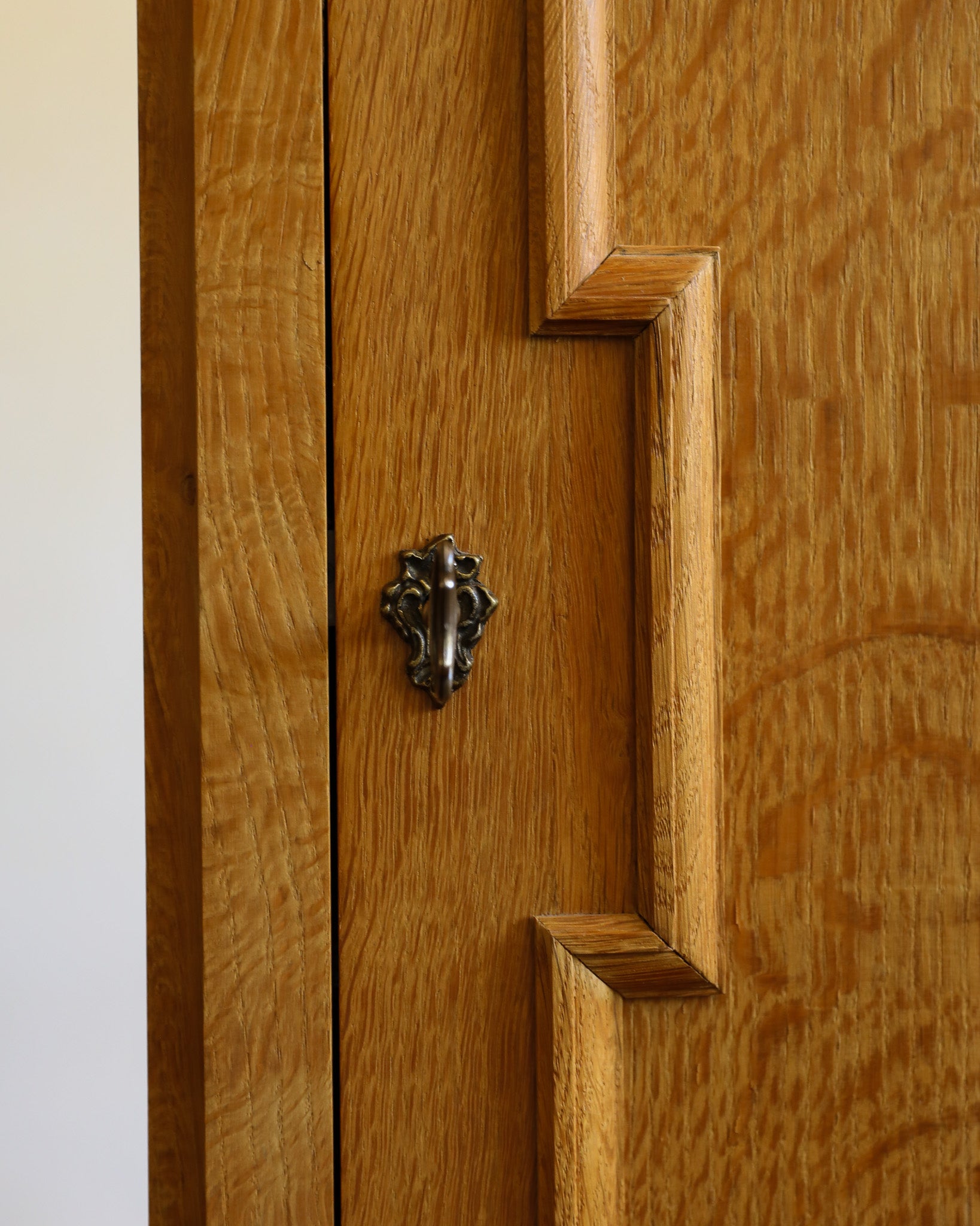 Close-up of a warm medium-brown wooden cabinet door with decorative raised paneling and a dark metal lion head knocker.