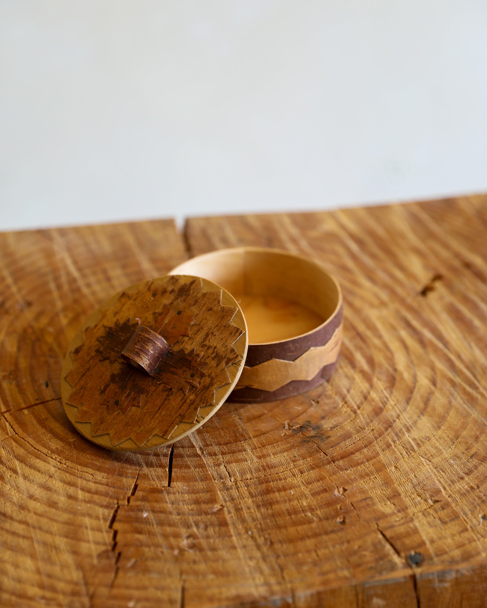 A small round wooden box with its lid off, placed on a rustic wooden surface against a plain light background.