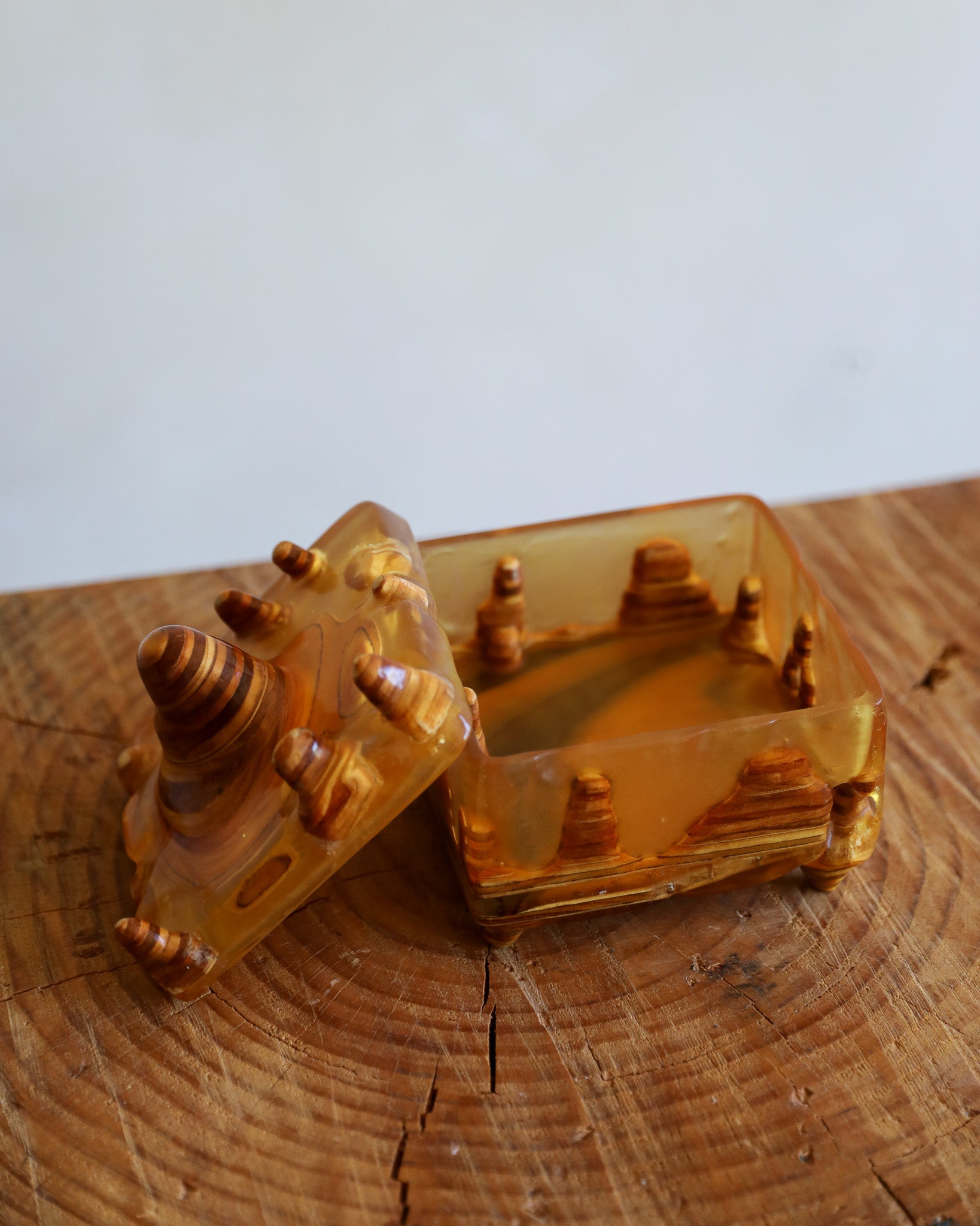 A translucent amber-colored resin box with a matching lid, featuring carved desert pyramid and dune motifs, displayed on a rustic wooden surface against a light gray background.