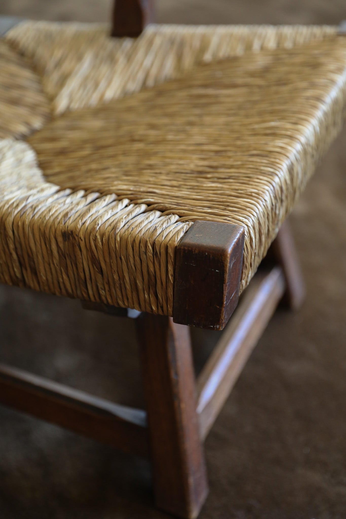 Close-up of a woven natural-fiber seat on a wooden chair, showing the texture of the rope and the dark brown wooden frame corner.