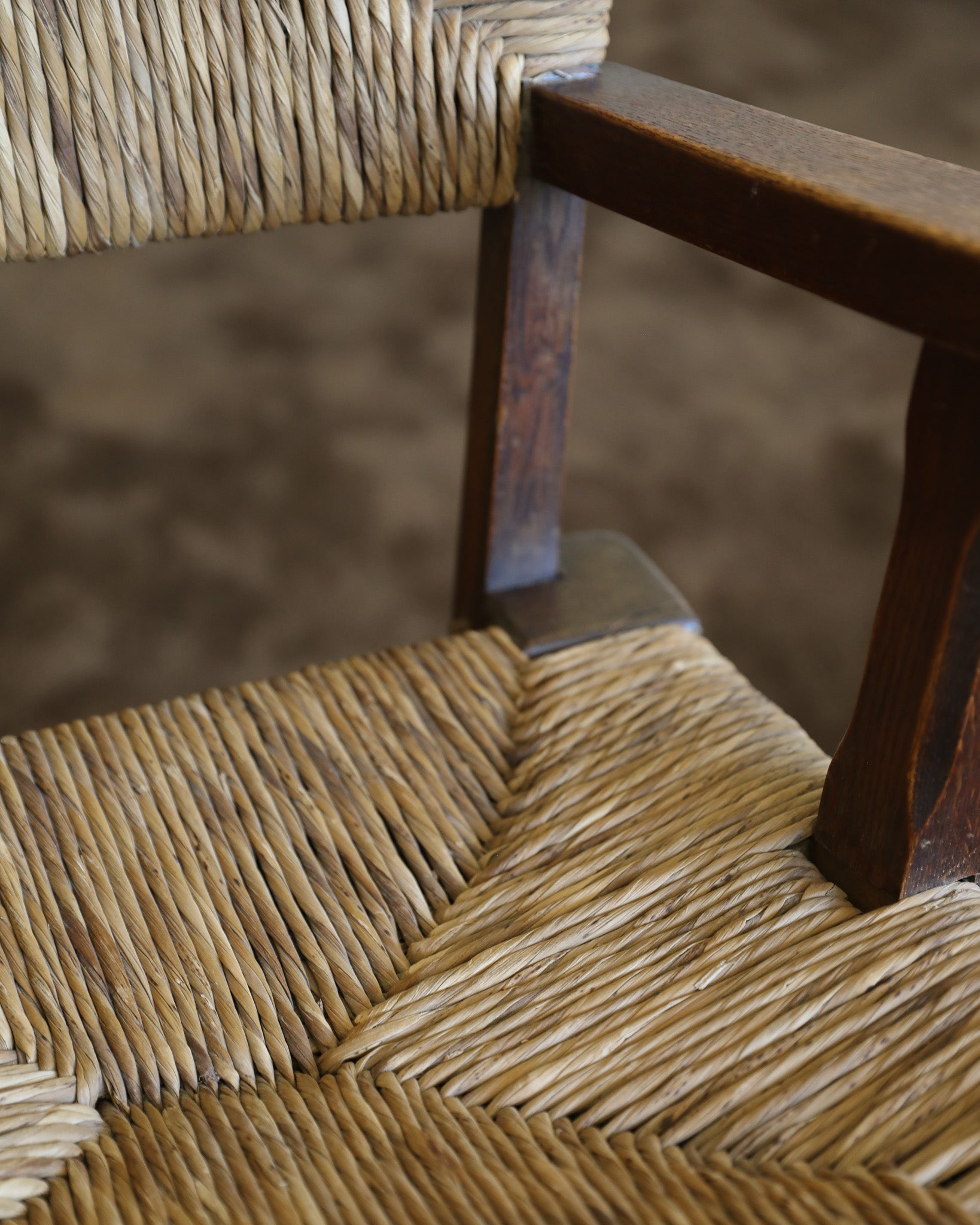 Close-up of a woven chair seat and back in natural straw with a dark brown wooden frame, showing the texture of the rope and wood.