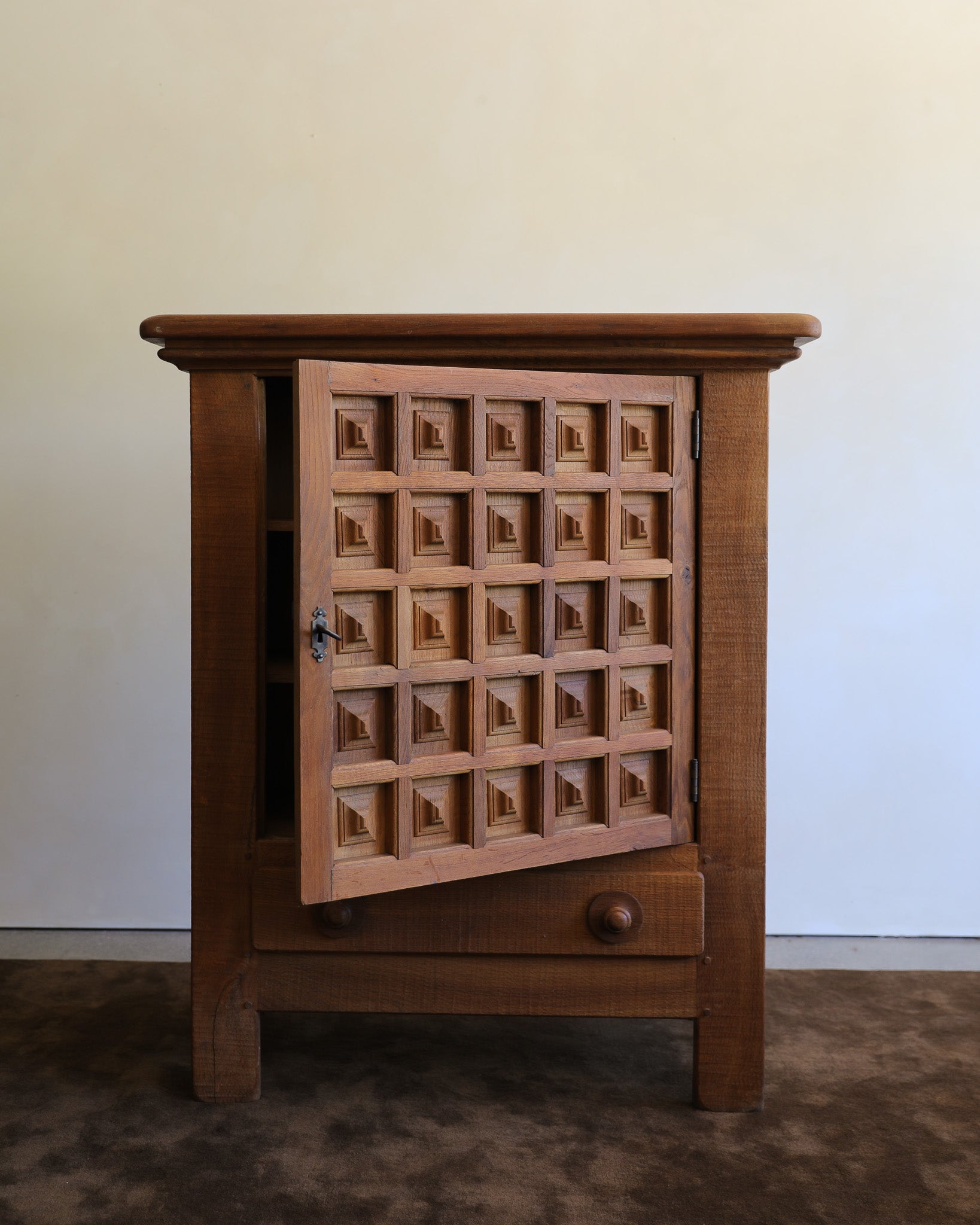 A small wooden cabinet with a carved door featuring a grid of small boat motifs, shown against a plain light wall and dark floor.