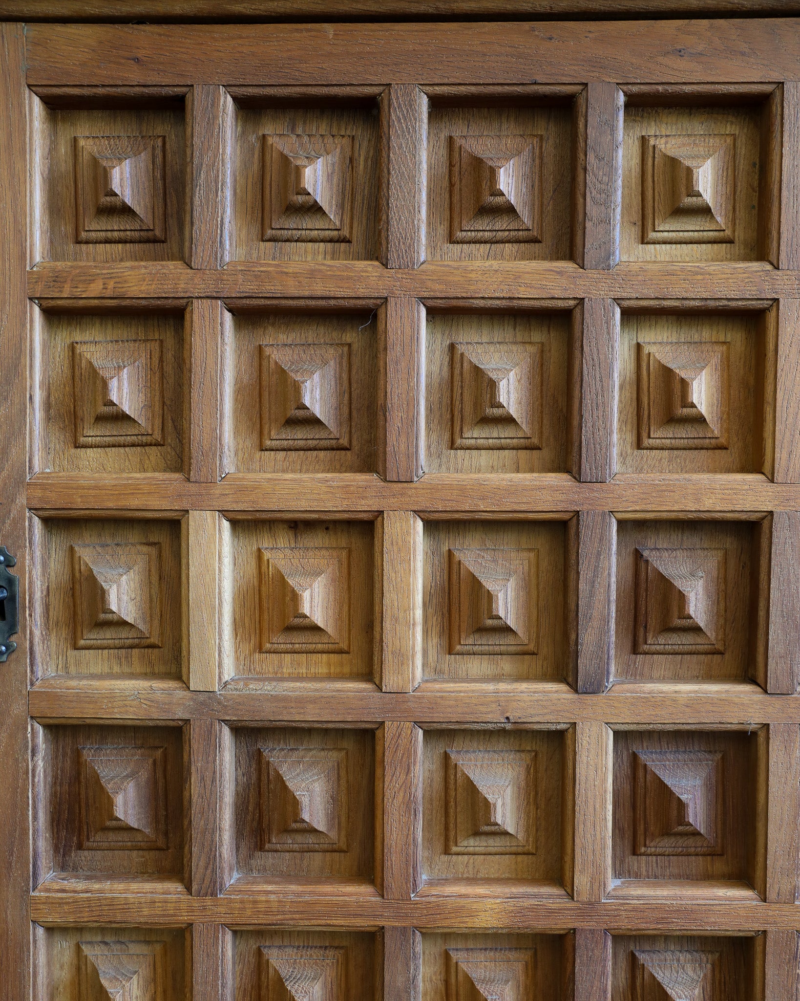 Close-up of a medium brown wooden door featuring a grid pattern of raised square panels with a geometric star-like design in the center of each panel.