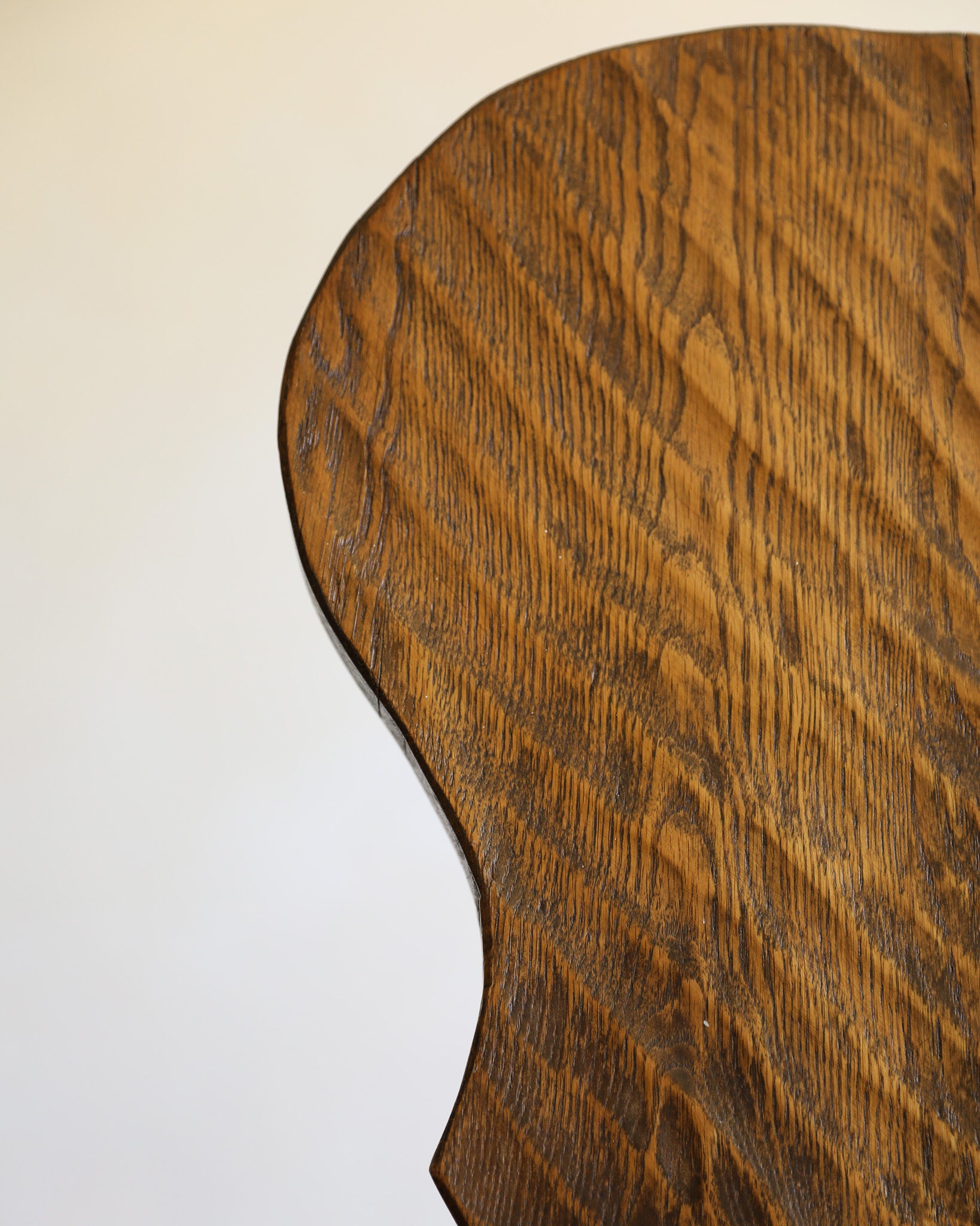 Close-up of a curved wooden chair with a prominent natural oak wood grain pattern, set against a plain off-white background.