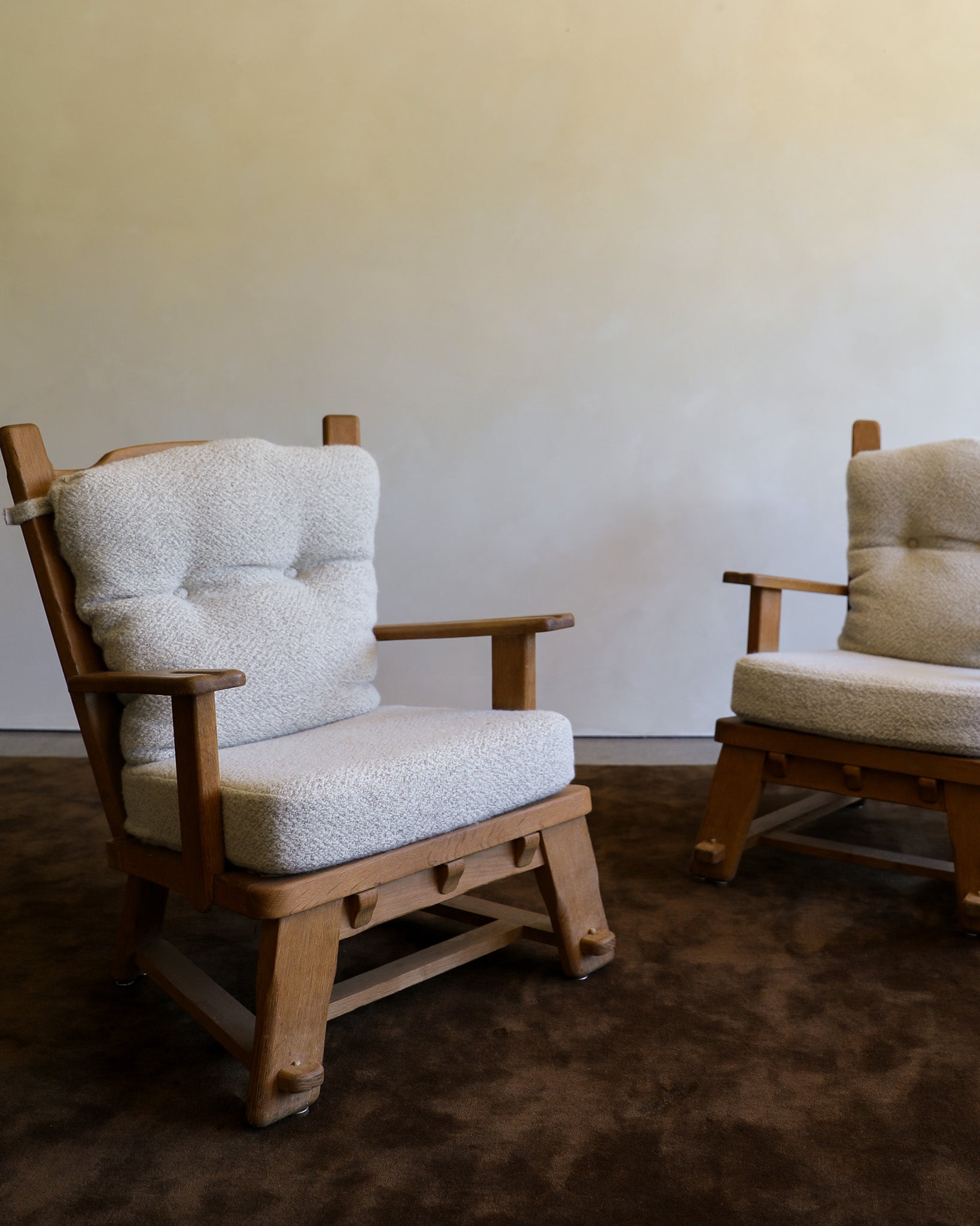 Two wooden chairs with tufted bouclé cushions in a neutral indoor setting with a brown rug and plain wall.