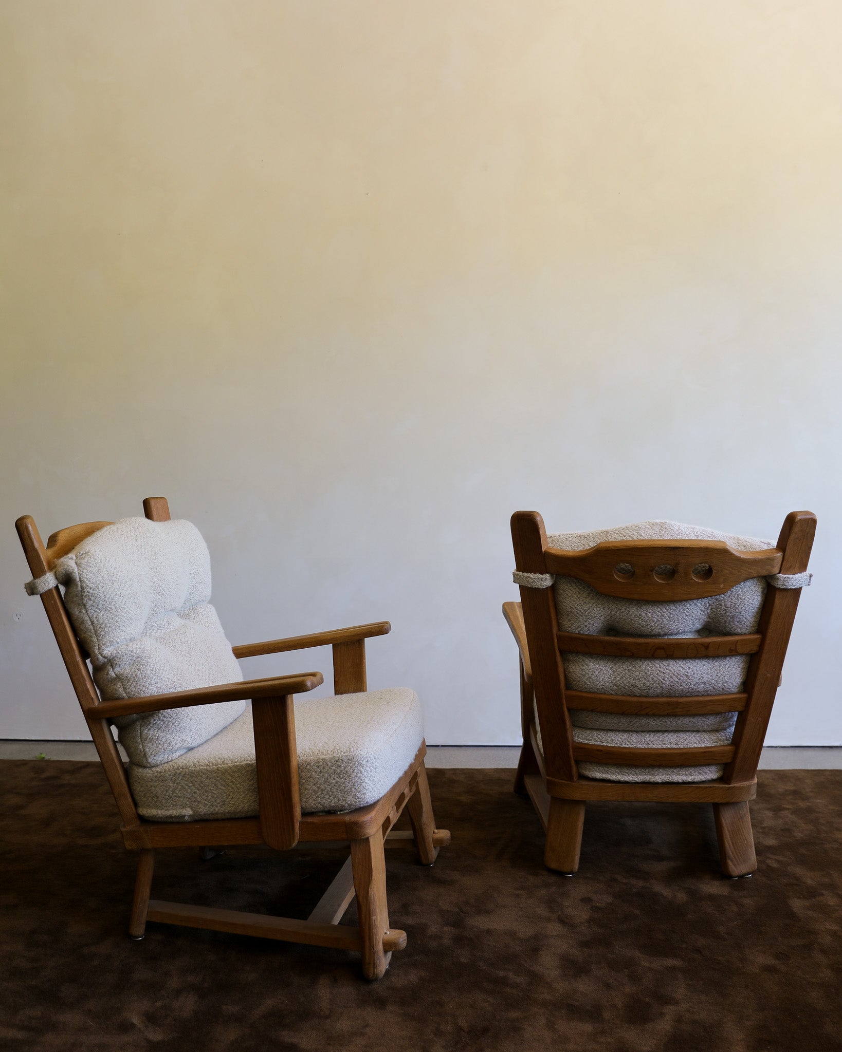 Two wooden chairs with tufted bouclé cushions in a neutral indoor setting with a brown rug and plain wall.