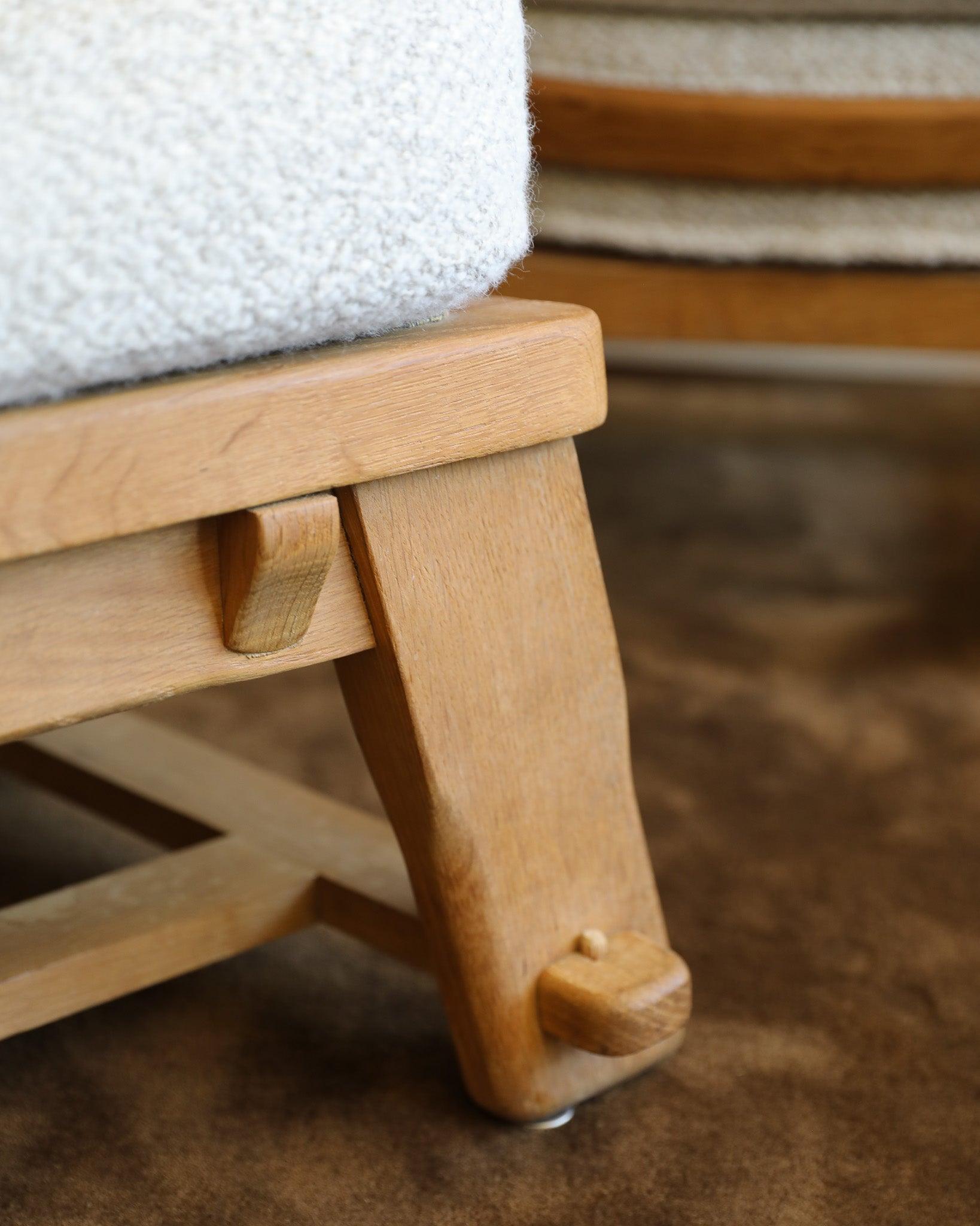 Close-up of a light natural wood stool or ottoman with a white textured cushion, shown on a brown carpeted floor.