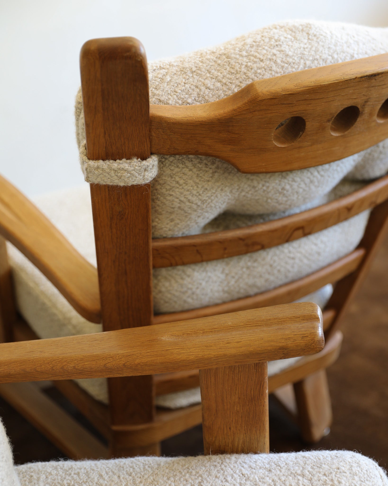 Two wooden chairs with tufted bouclé cushions in a neutral indoor setting with a brown rug and plain wall.