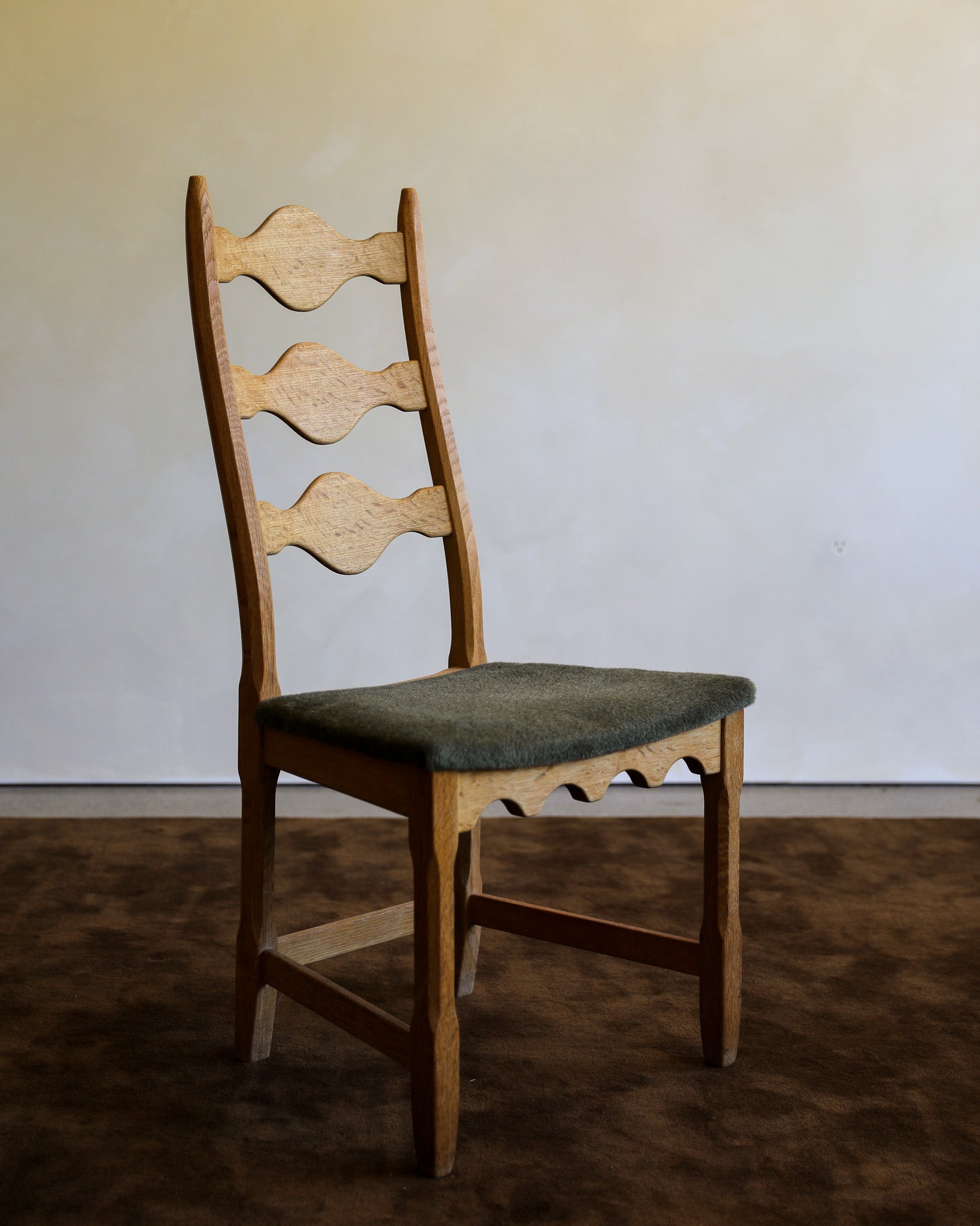 Henning Kjærnulf Razor Back Dining Chair with green suri alpaca upholstered seat on chocolate brown wool rug with warm lime wash background