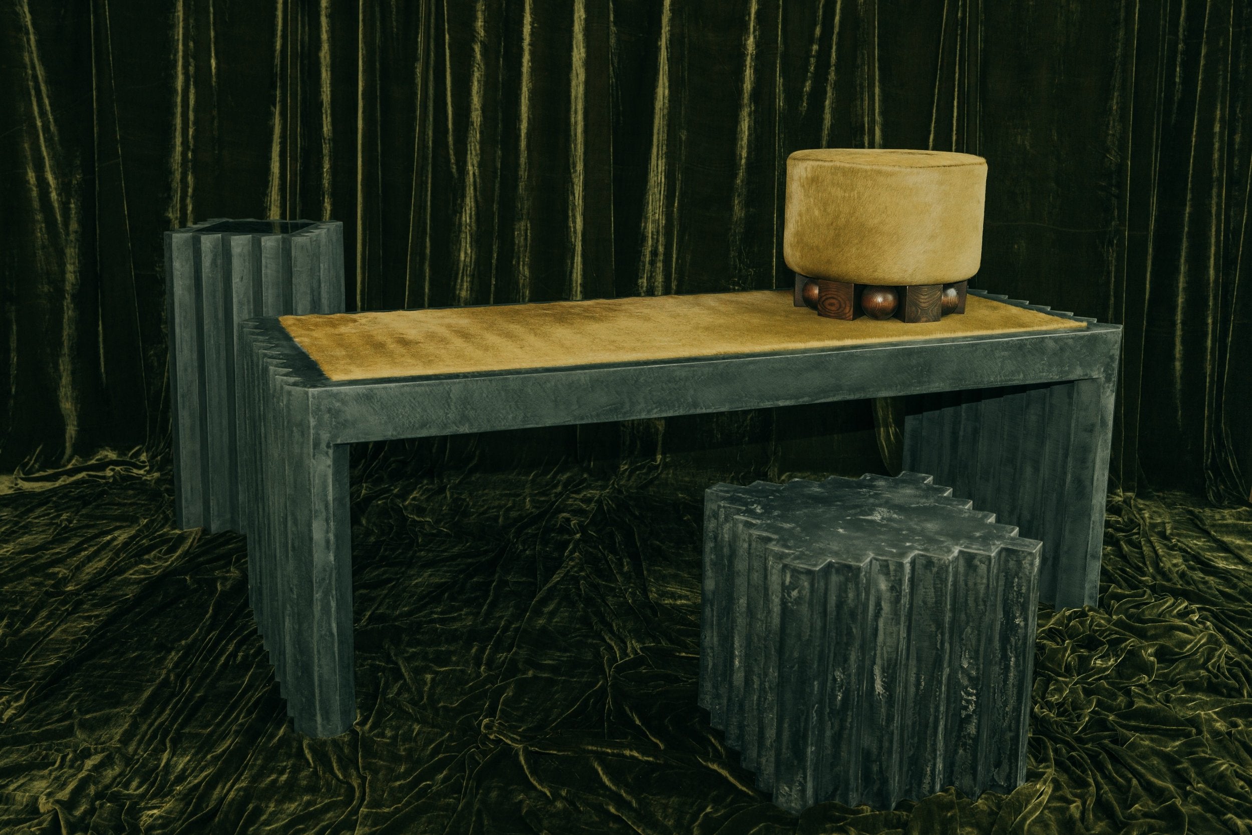 haus of hommeboys green faceted plaster side table with matching desk and pillar and green hide pouf on green velvet backdrop