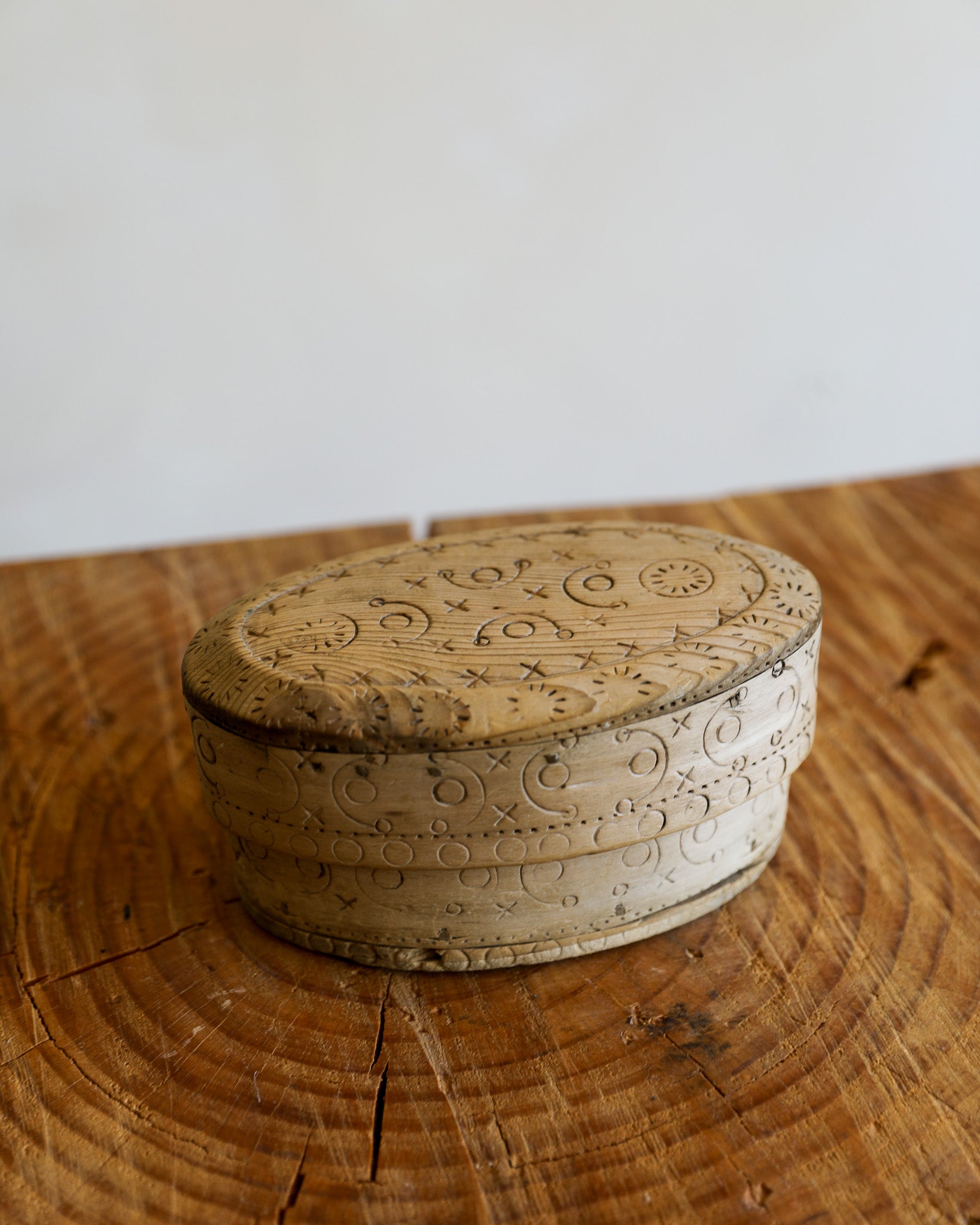 An oval-shaped carved wooden box with intricate floral and scroll engravings, resting on a rustic wooden surface against a plain light background.