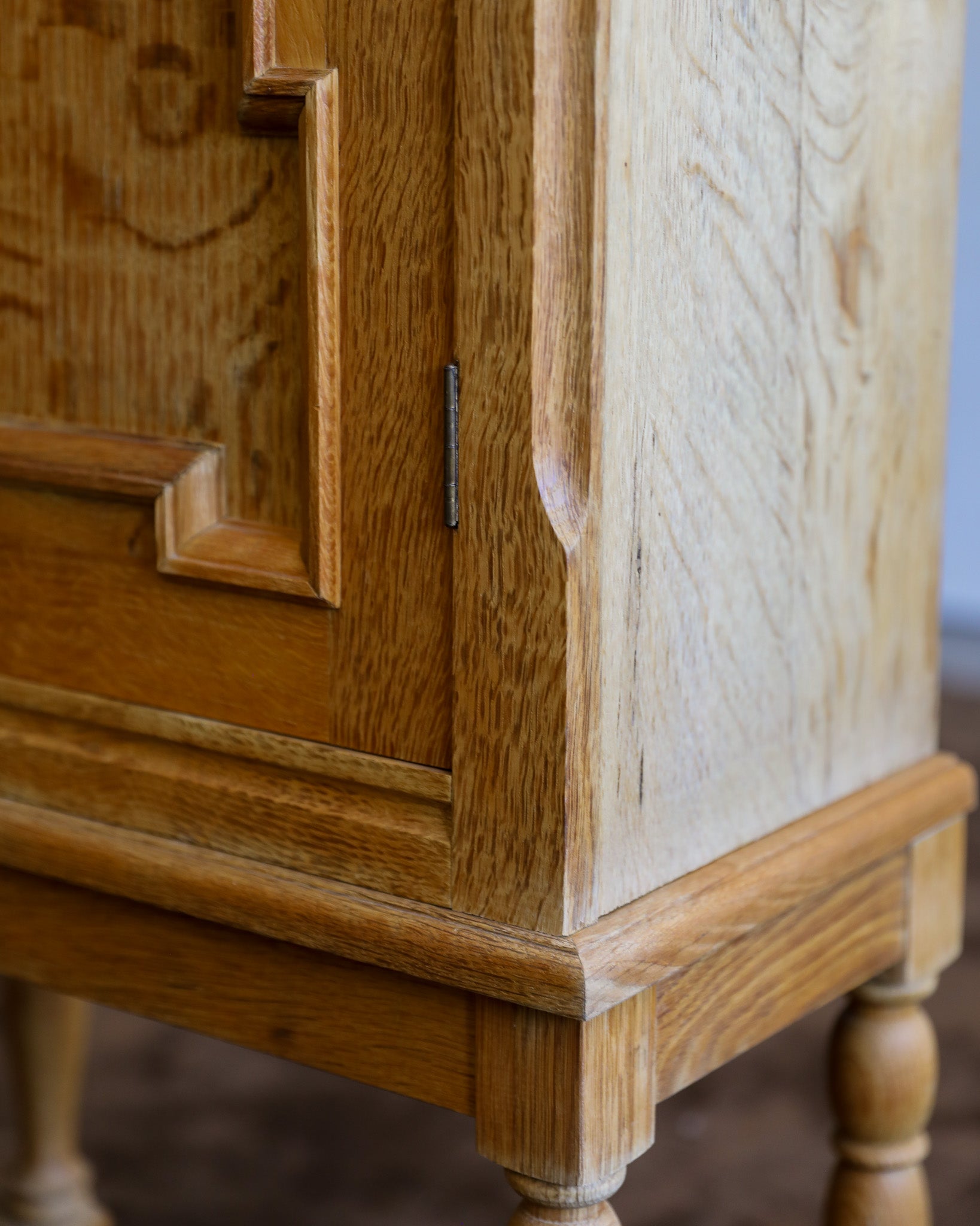 Close-up of a light oak wood cabinet corner showing the grain, beveled edges, and turned legs.