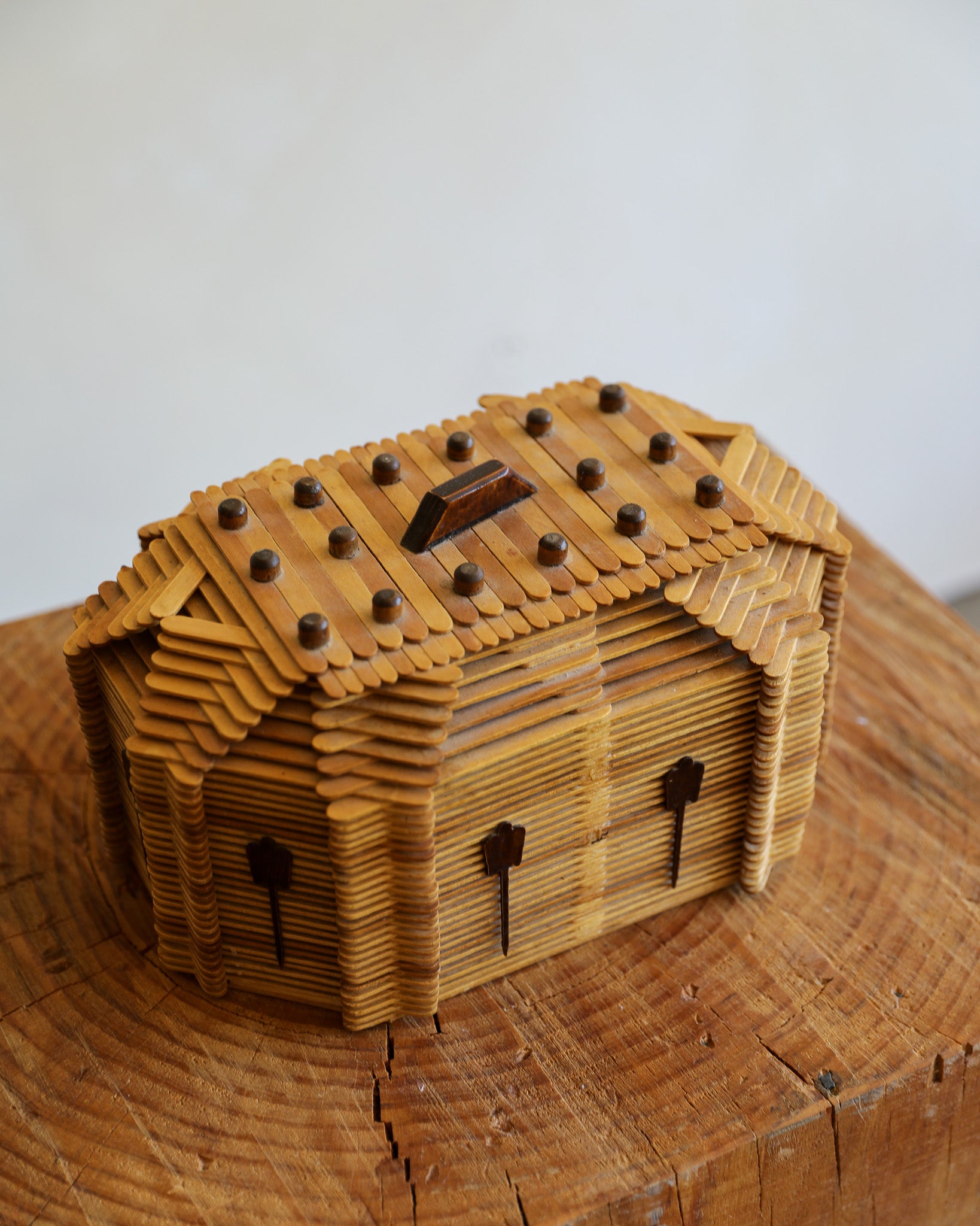 A small wooden house-shaped box made from layered wood slices, photographed on a wood surface against a plain light background.