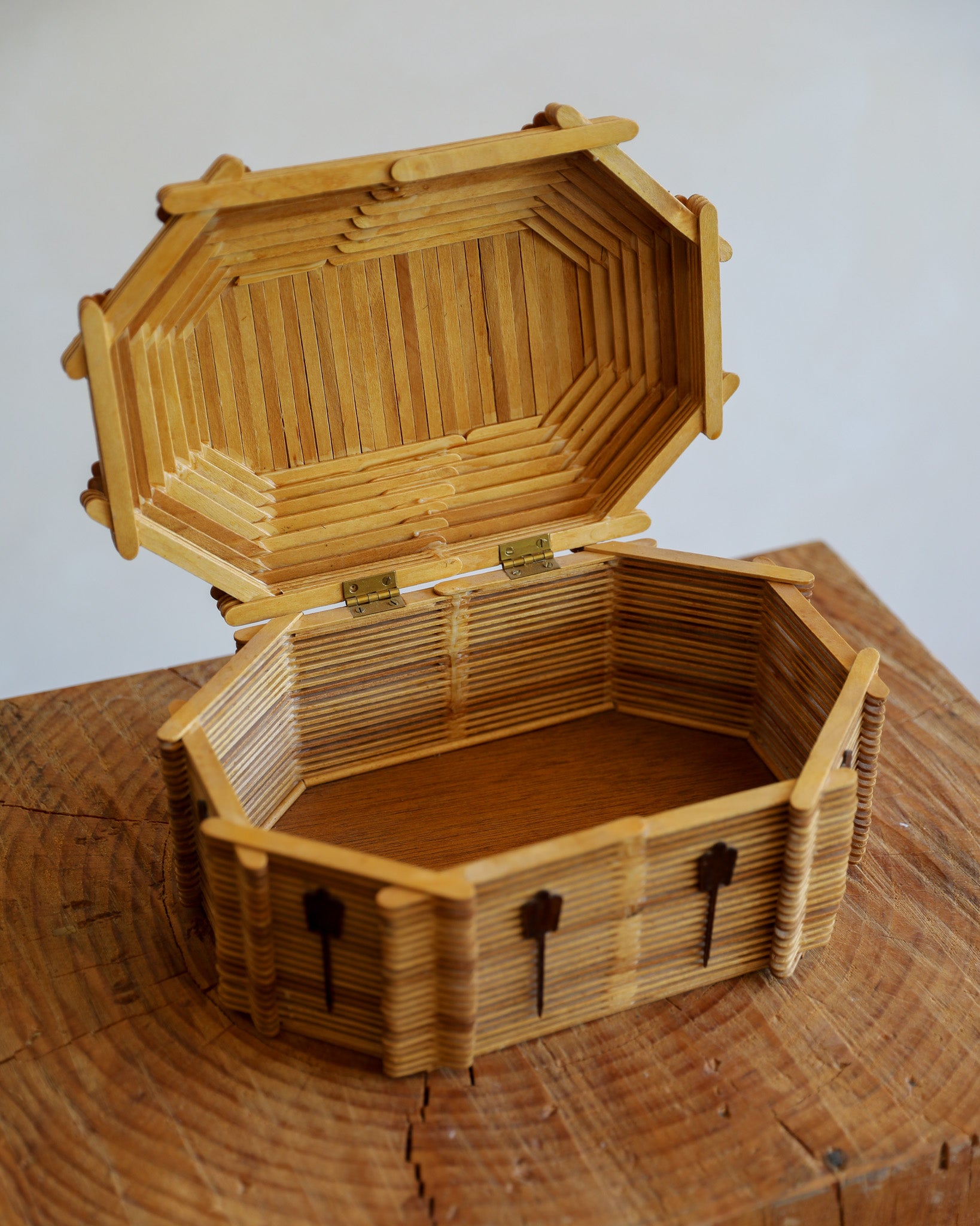 an open tramp art box made of popsicle sticks on a wood stump