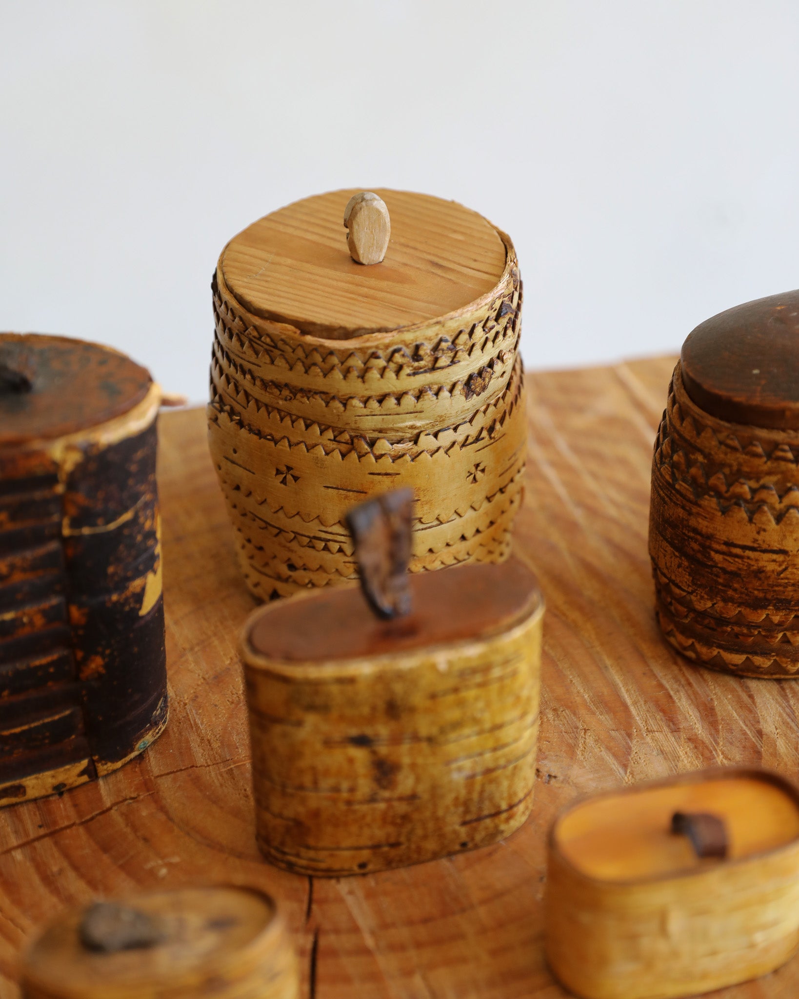 A group of small handcrafted wooden containers with lids, displayed on a rustic wooden surface against a plain white background.