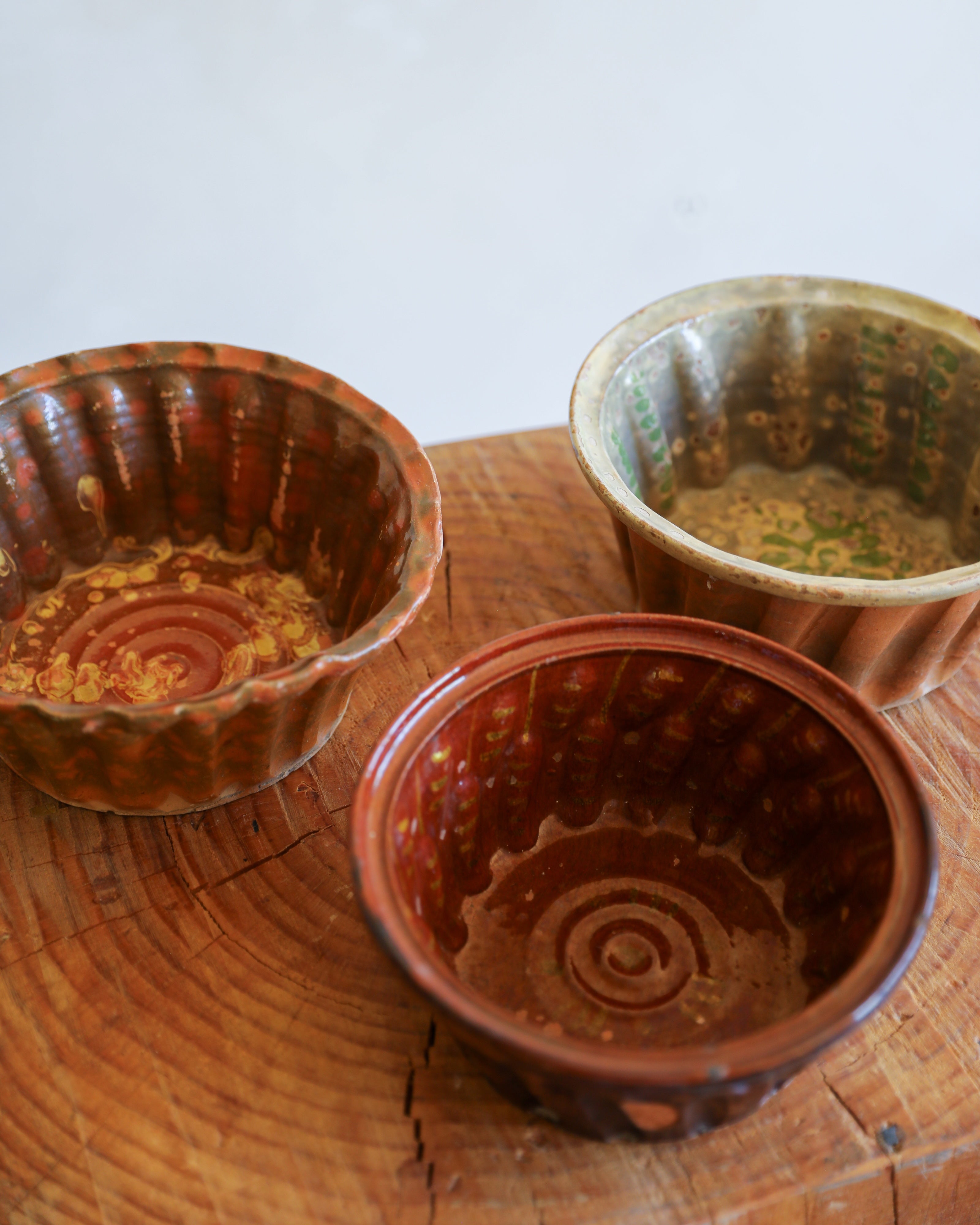 Three small decorative ceramic bowls with scalloped flared rims and concentric spiral patterns inside, displayed on a rustic wooden slice against a light background.