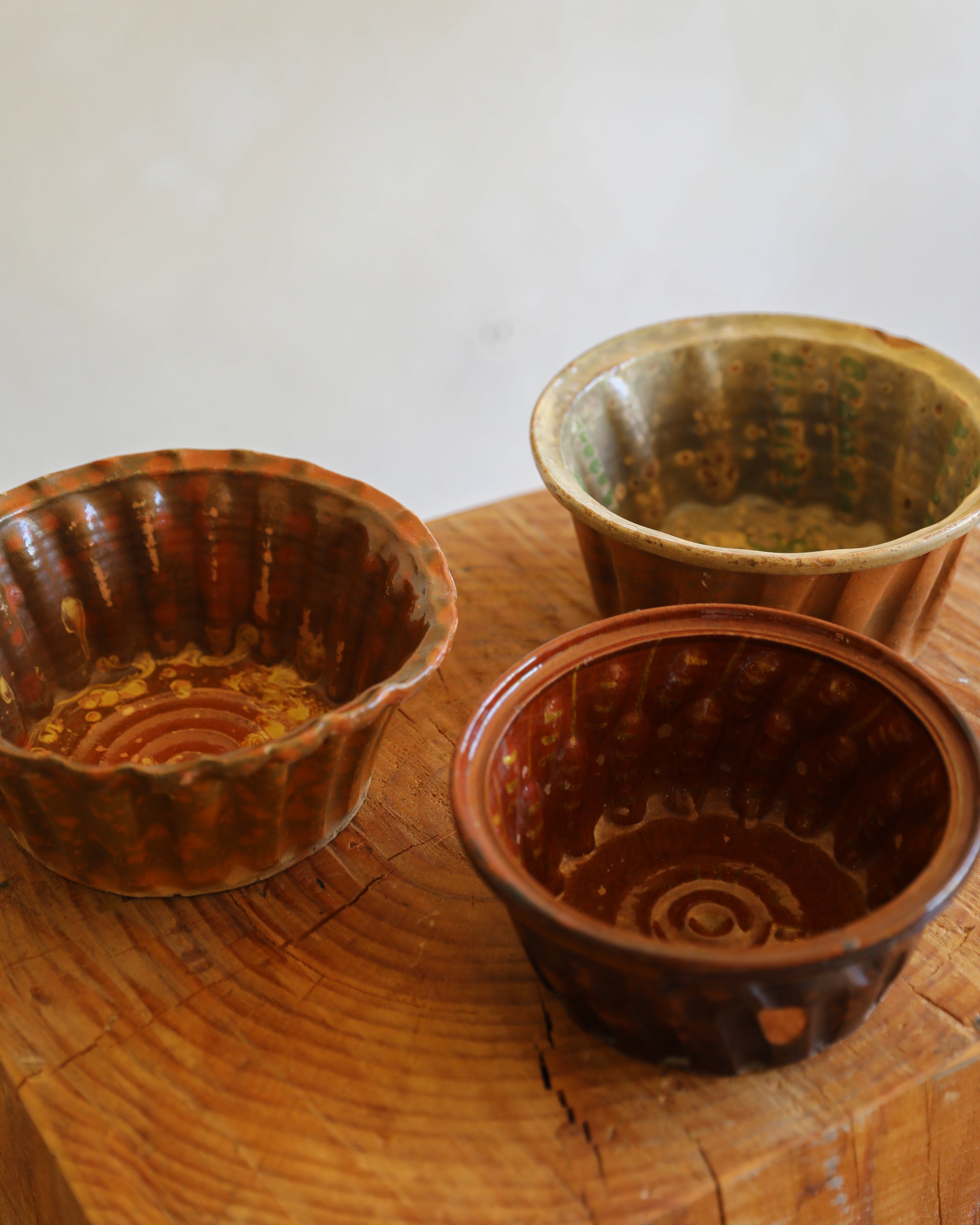 Three small rustic ceramic bowls with scalloped flared rims, shown on a wooden surface against a plain light background.